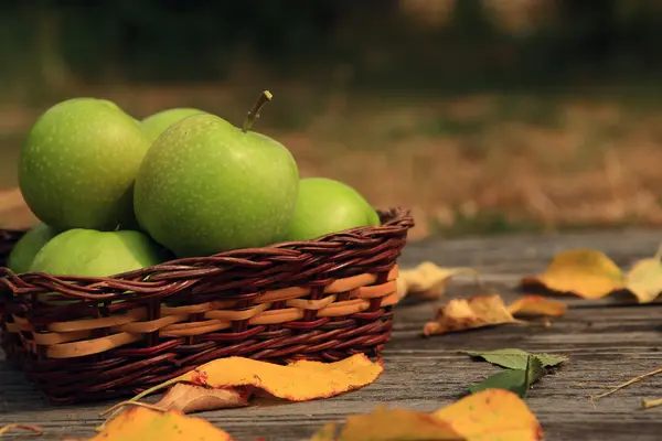 Яблоко на деревянном столе с опавшими осенними листьями — стоковое фото