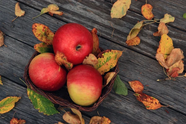 Яблоко на деревянном столе с опавшими осенними листьями — стоковое фото