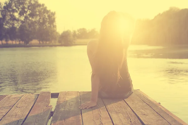 放松年轻的女子，在木码头在湖在日落的旧照片 — 图库照片