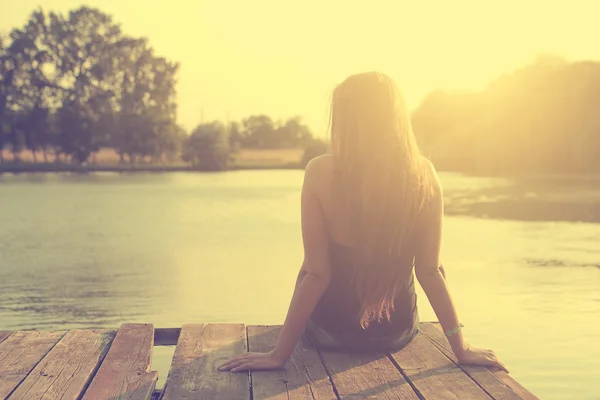 Vintage foto de relaxante jovem mulher no cais de madeira no lago ao pôr do sol — Fotografia de Stock