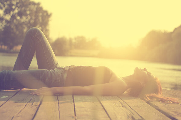 Vintage photo of relaxing young woman on wooden pier at the lake in sunset