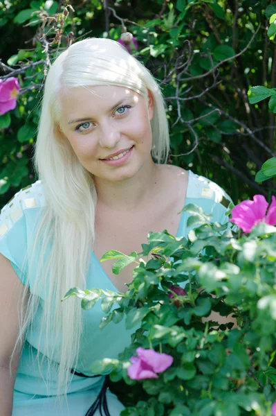 Blondine posiert in der Nähe des Busches mit Blumen — Stockfoto