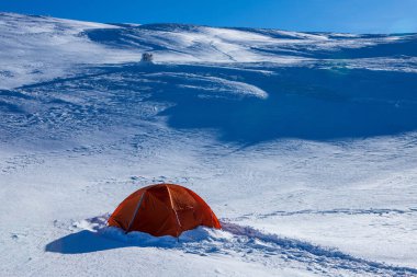Dağların yamaçlarında karla kaplı bir turist çadırı.