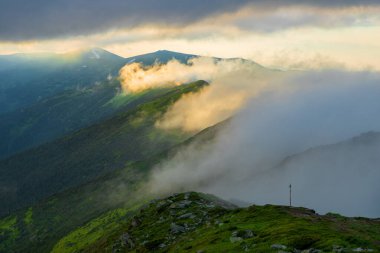 Akşam güneşiyle aydınlanan sis, dağların yamaçlarını kaplıyor. Karpatlar, Ukrayna.