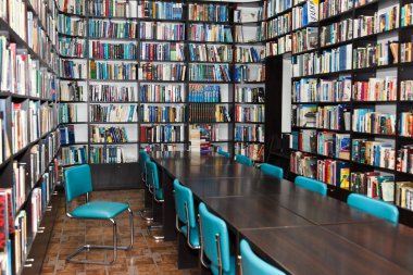 Kütüphanedeki okuma odasında raflarda bir sürü renkli kitap var.