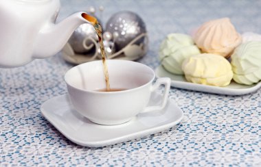 Çay partisi zamanı. Ev sahibi çaydanlıktan fincanlara çay doldurur. Lezzetli taze marşmelovlarla dolu bir parça. Şenlik masasında.