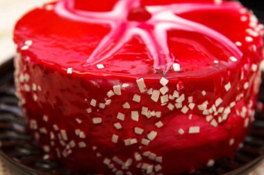 Drunk Cherry cake, a delicious, sweet confection with red white glaze, white chocolate crumbs and cherries lies on table.Side view