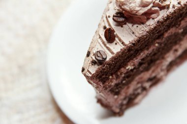 Portion of tasty, original, sweet coffee cake covered with glaze and coffee beans lies in a dessert plate on a table
