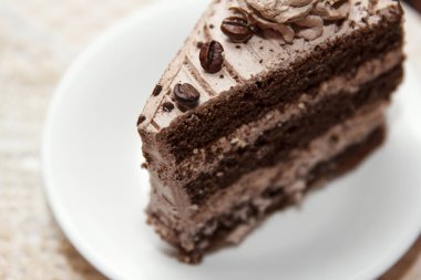 Portion of tasty sweet coffee cake covered with glaze and coffee beans lies in a dessert plate on a table