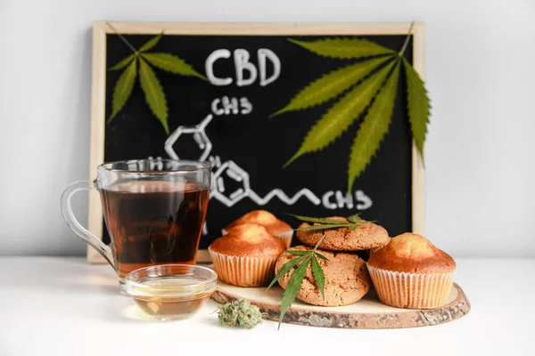 Muffins und Kekse mit CBD-Cannabis und Blattgarnitur. Arzneimittel. Medizinische Marihuana-Behandlung für den menschlichen Konsum. Gegen eine Tafel mit CBD-Hanfform. Stockbild