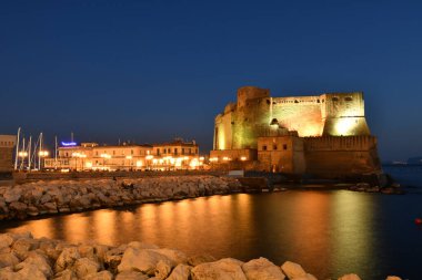 Napoli, İtalya, 03 / 10 / 2022. Castel Dell 'Ovo' nun gece manzarası, şehrin rıhtımına inşa edilmiş bir ortaçağ kalesi. Bina küçük bir adada duruyor ve dar bir köprü ile anakaraya bağlı..