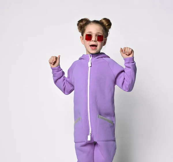 Piccola bambina in una calda tuta sportiva blu su uno sfondo grigio. Carina la ragazzina che guarda la telecamera. Moda sportiva per bambini. — Foto Stock