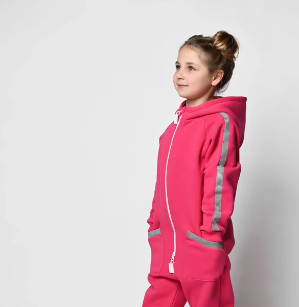 Half-length portrait A happy stylish girl in a sports pink suit stands with her hands in her pockets, looks to the side. stylish cotton tracksuit, pajamas with a hood, a fashion model for children — Stock Fotó