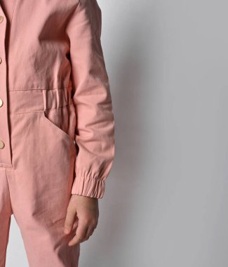 Çocuğa yakın çekim. Üzerinde çiviler olan sıradan bir pamuk tulum. Gri bir arka planda izole edilmiş pantolonlu bir çocuğun fotoğrafı. Çocuk kıyafetleri reklamı.