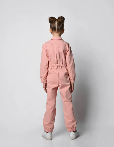 Vista trasera Foto de perfil de longitud completa de una chica positiva de pie en zapatillas blancas y un mono de algodón rosa sobre un fondo claro Fotos de stock
