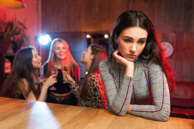 Sad bored girl at a party on the background of dancing and drinking friends.