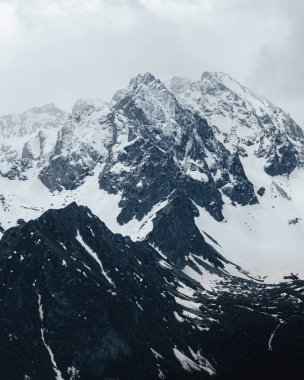Dağın tepesinde kar, sisli gökyüzünün ve kış dağlarının güzel fotoğrafları. Açık hava manzarası, kayalık uçurum. Kış Turizmi.