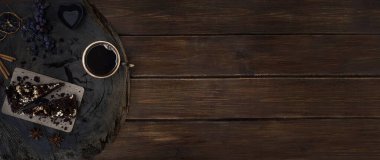 Tahta bir meşe kesiminde çikolatalı kek dilimleri, limon dilimleri, üzüm, tarçın, anason, anason ve kalp şeklinde şık bir şamdan. Kahverengi ahşabın kopyalama alanı ile üst görünüm
