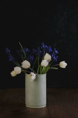 Taze bir buket beyaz şakayık ve ahşap arka planda teneke bir kutuda mavi muscari çiçekleri.