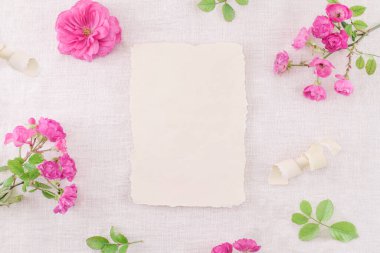 El ilanı, keten peçetenin üzerinde pembe güller olan boş tebrik kartı maketi. Düğün, doğum günü kırtasiyesi. Üst görünüm.