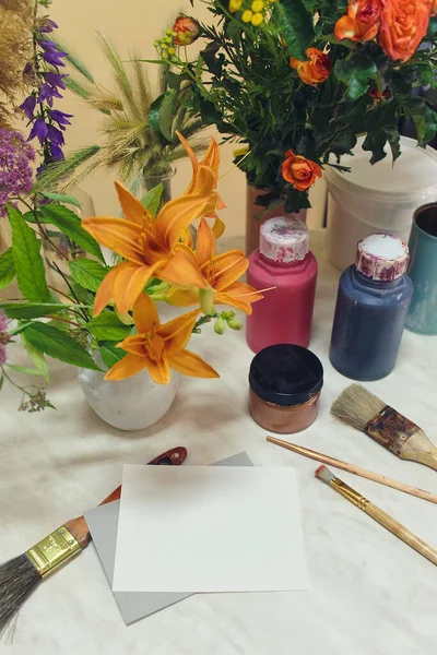 Creative workshop. Paints, brushes, flowers, blank form on a marble table. View from above.