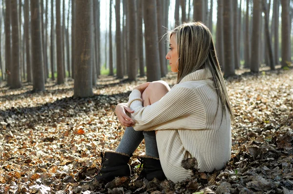 Beautiful blonde sitting on leaves in a forest of poplars — Stock Photo, Image
