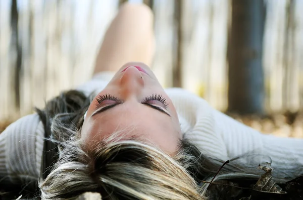 Beautiful blonde girl lying on leaves in a forest of poplars — Stock Photo, Image