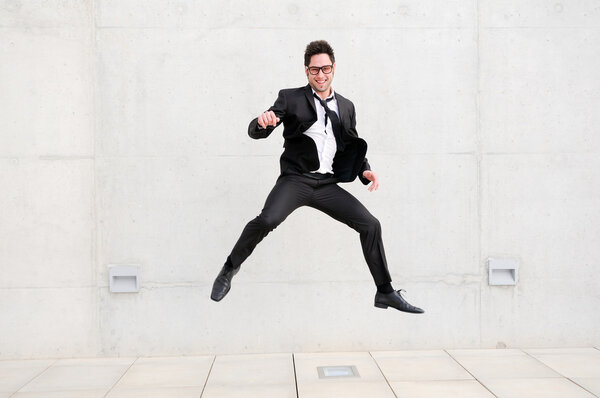 Молодой красивый бизнесмен в очках прыгает по улице
