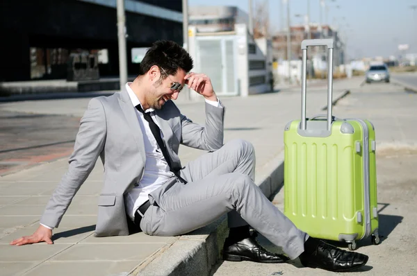 Man dressed in suit and suitcase sitting on the floor in the str