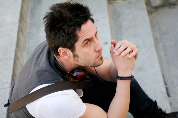 Retrato de un joven pensativo sentado en las escaleras, con auriculares — Foto de Stock