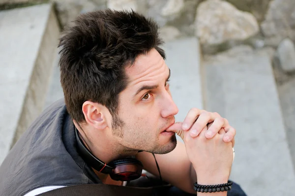 Porträt eines nachdenklichen jungen Mannes, der mit Kopfhörern auf Stufen sitzt — Stockfoto