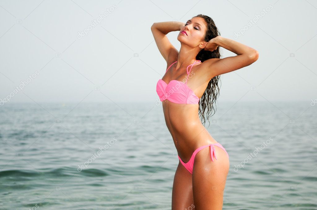 Young woman with beautiful body on a beach in a pink bikini Stock