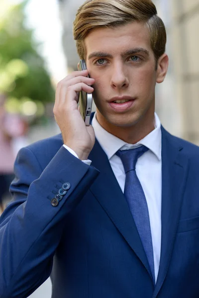 Привлекательный молодой бизнесмен на телефоне на городском фоне — стоковое фото