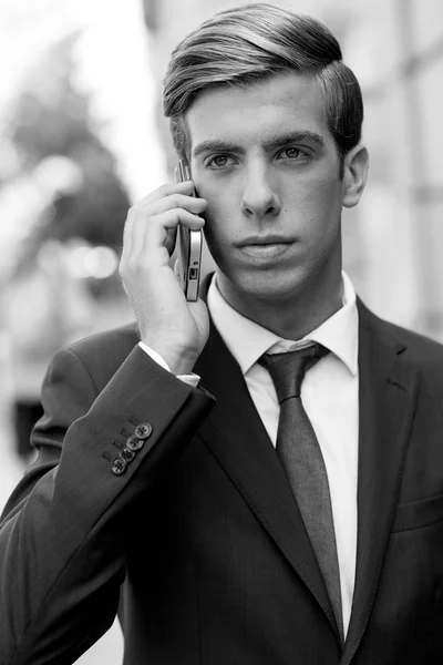 Jovem empresário atraente ao telefone em fundo urbano — Fotografia de Stock