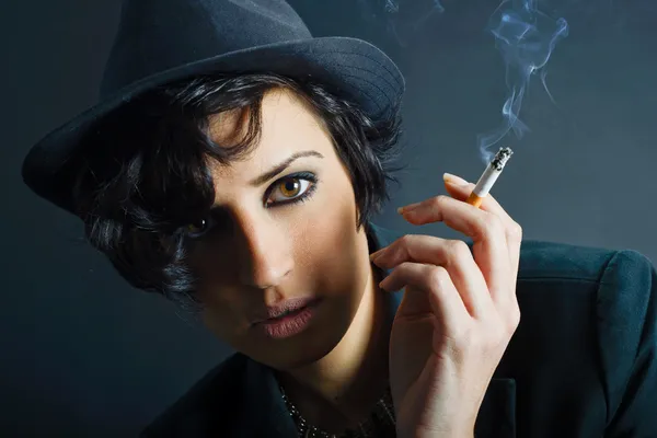 Brunette woman smoking a cigarette on black background wearing a — Stock Photo, Image