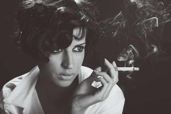 Mulher morena elegante fumando um cigarro no fundo preto — Fotografia de Stock