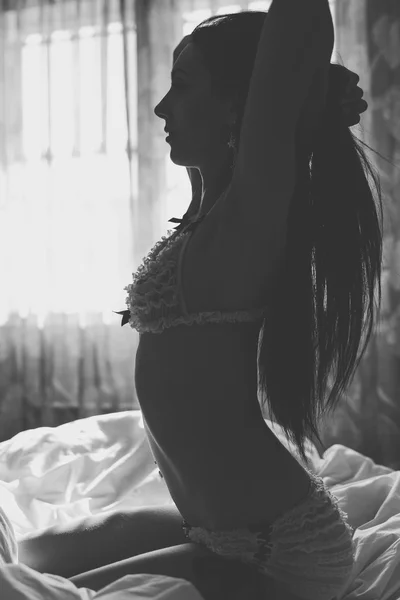 Yatakta iç çamaşırlarıyla poz veren seksi genç kadın. — Stok fotoğraf