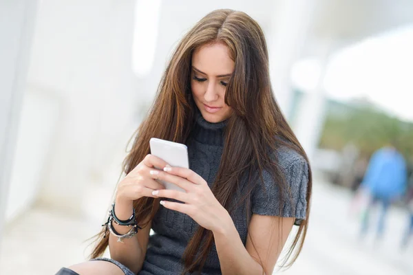 Bella giovane donna in sfondo urbano scrivere con uno smartp — Foto Stock