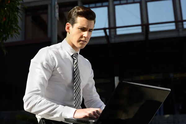 Junger Geschäftsmann tippt in einem Laptop-Computer im urbanen Hintergrund — Stockfoto