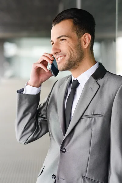 Jovem empresário atraente ao telefone em um prédio de escritórios — Fotografia de Stock