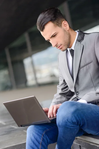 Joven hombre de negocios escribiendo en un ordenador portátil en el fondo urbano — Foto de Stock