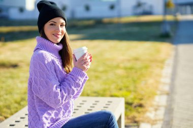 Bayan öğrenci kahve molası veriyor. Kolejinin önündeki bankta oturuyor..