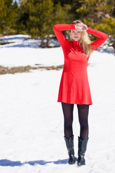 Giovane donna bionda indossa un vestito rosso e calze nere nelle montagne innevate in inverno. — Foto Stock