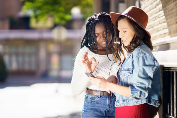 Två vänner tittar på sin smartphone tillsammans. Multietniska kvinnor. — Stockfoto