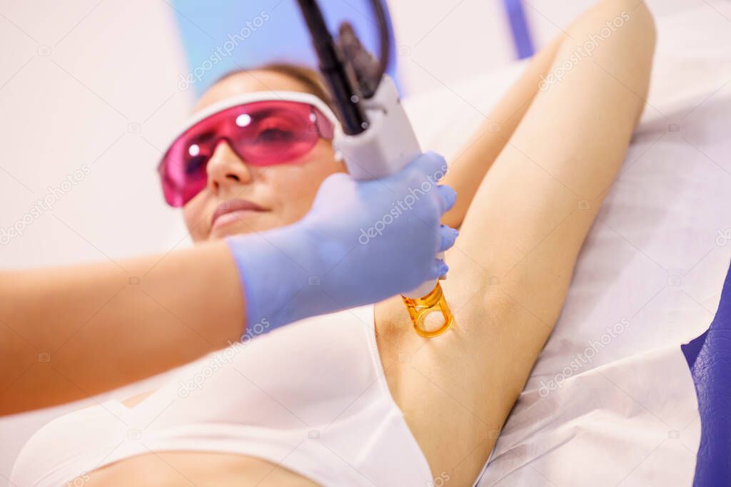 Woman receiving underarm laser hair removal at a beauty center.