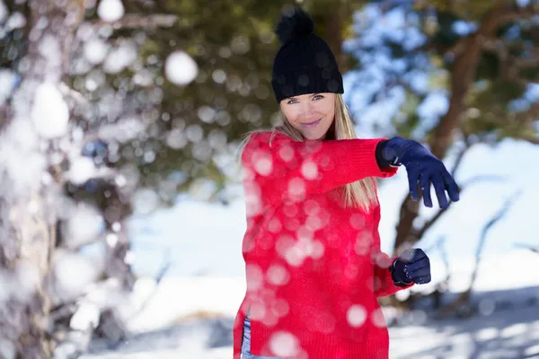 Szőke nő hógolyókat dobál előre egy hófödte erdőben a hegyekben. — Stock Fotó