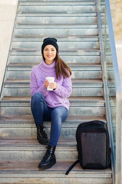 Kvinna i tjugoårsåldern tar en kaffepaus sittandes på några trappsteg på gatan. — Stockfoto