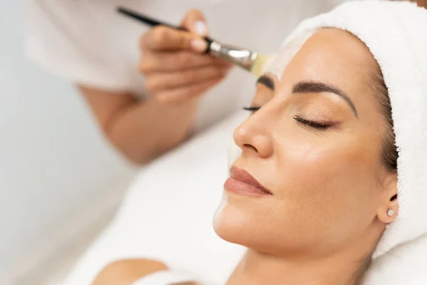 Estética aplicando una máscara a la cara de una mujer de mediana edad en un moderno centro de bienestar. — Foto de Stock