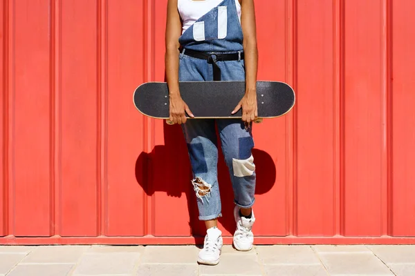 Unerkennbare Frau hält Skateboard mit den Händen an roter Stadtmauer. — Stockfoto