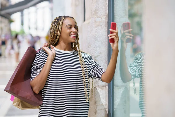 Joven mujer negra fotografiando un escaparate en una calle comercial con su smartphone. —  Fotos de Stock